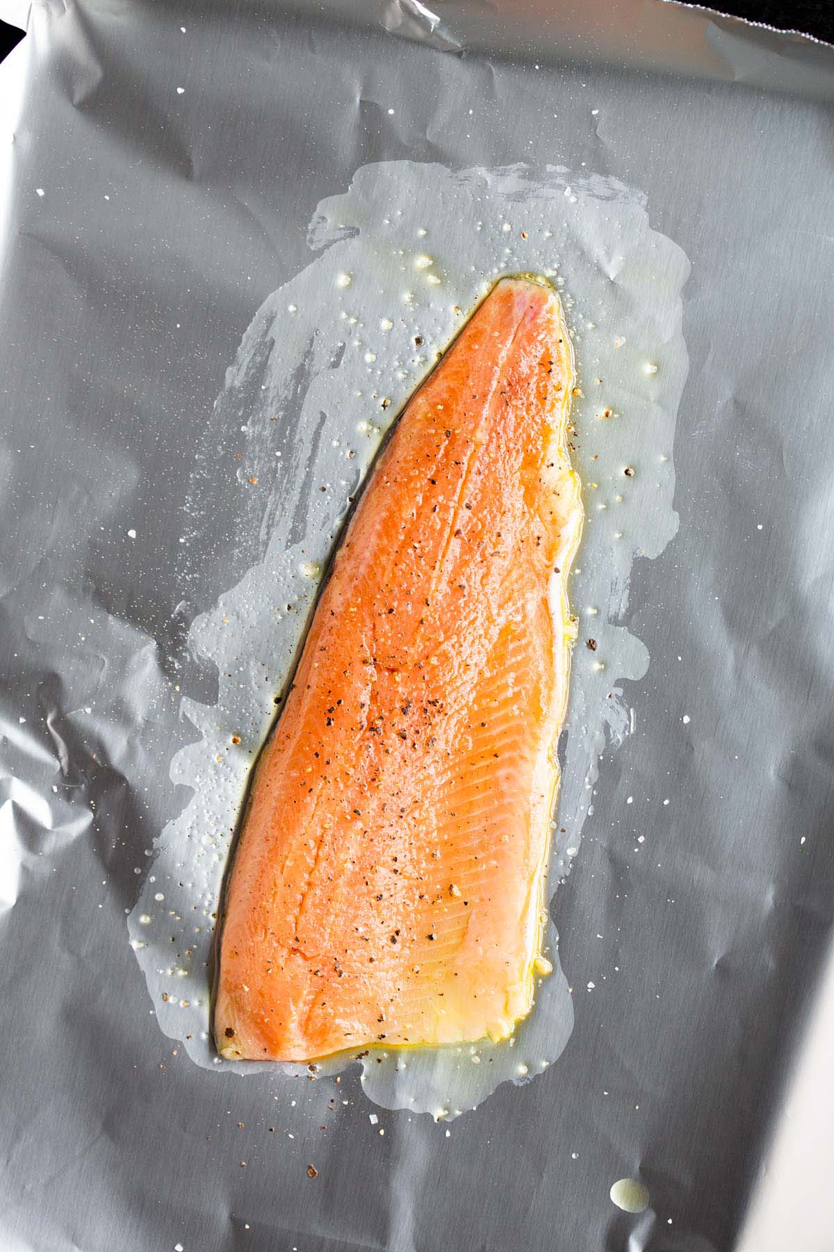 Uncooked rainbow trout on a sheet pan with olive oil.