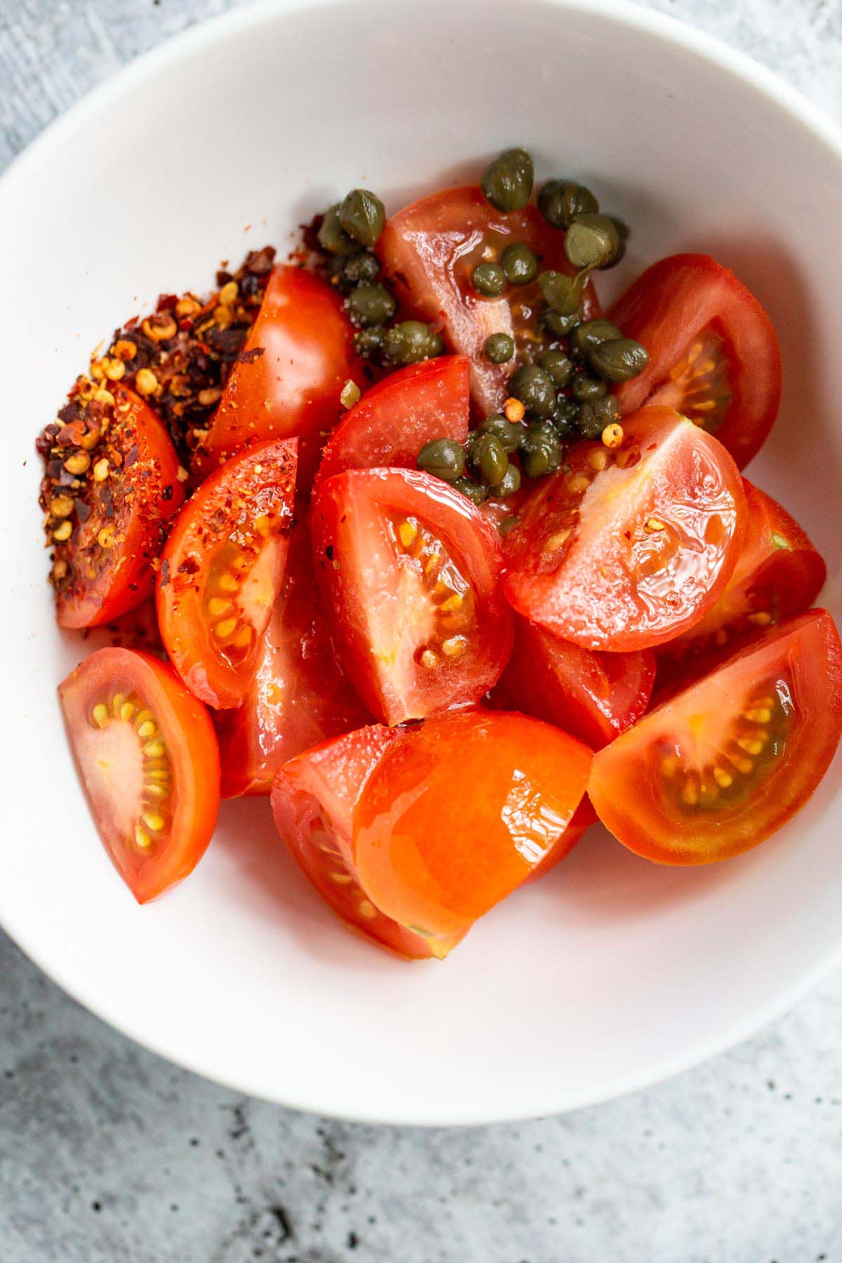 Tomatoes, capers, olive oil, and red pepper flakes in a bowl.