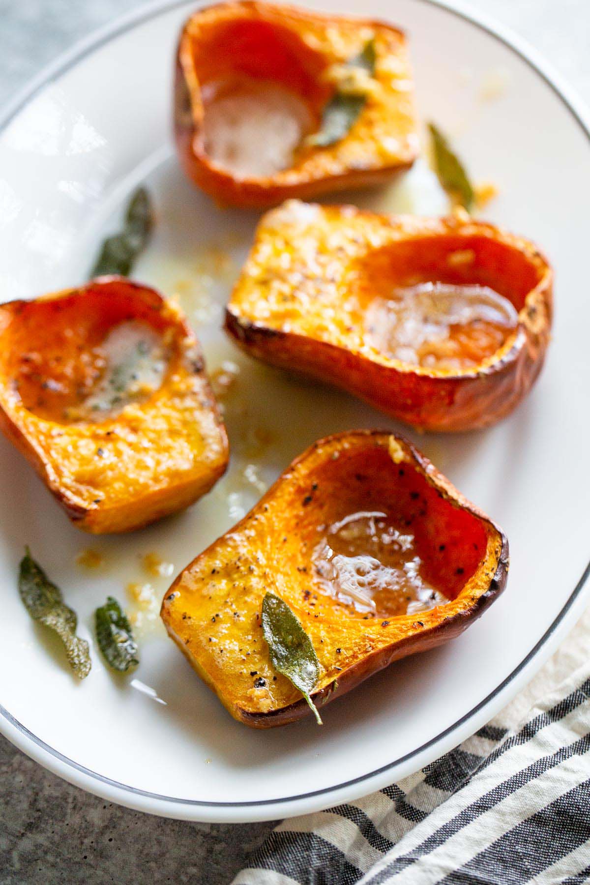 Honeynut squash topped with sage garlic butter on a white plate.