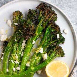 Air fryer broccolini topped with feta and lemon zest served with half a lemon.