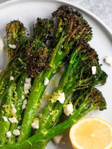 Air fryer broccolini topped with feta and lemon zest served with half a lemon.