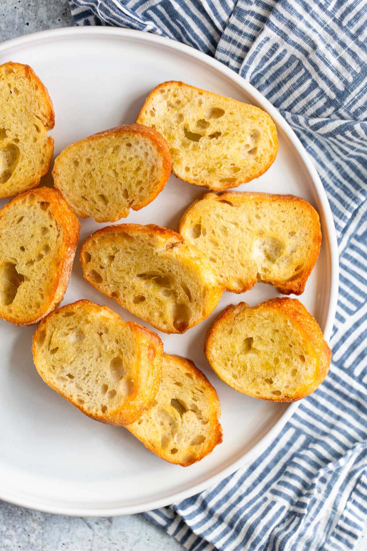 Crostini on a white plate with a white and blue towel.