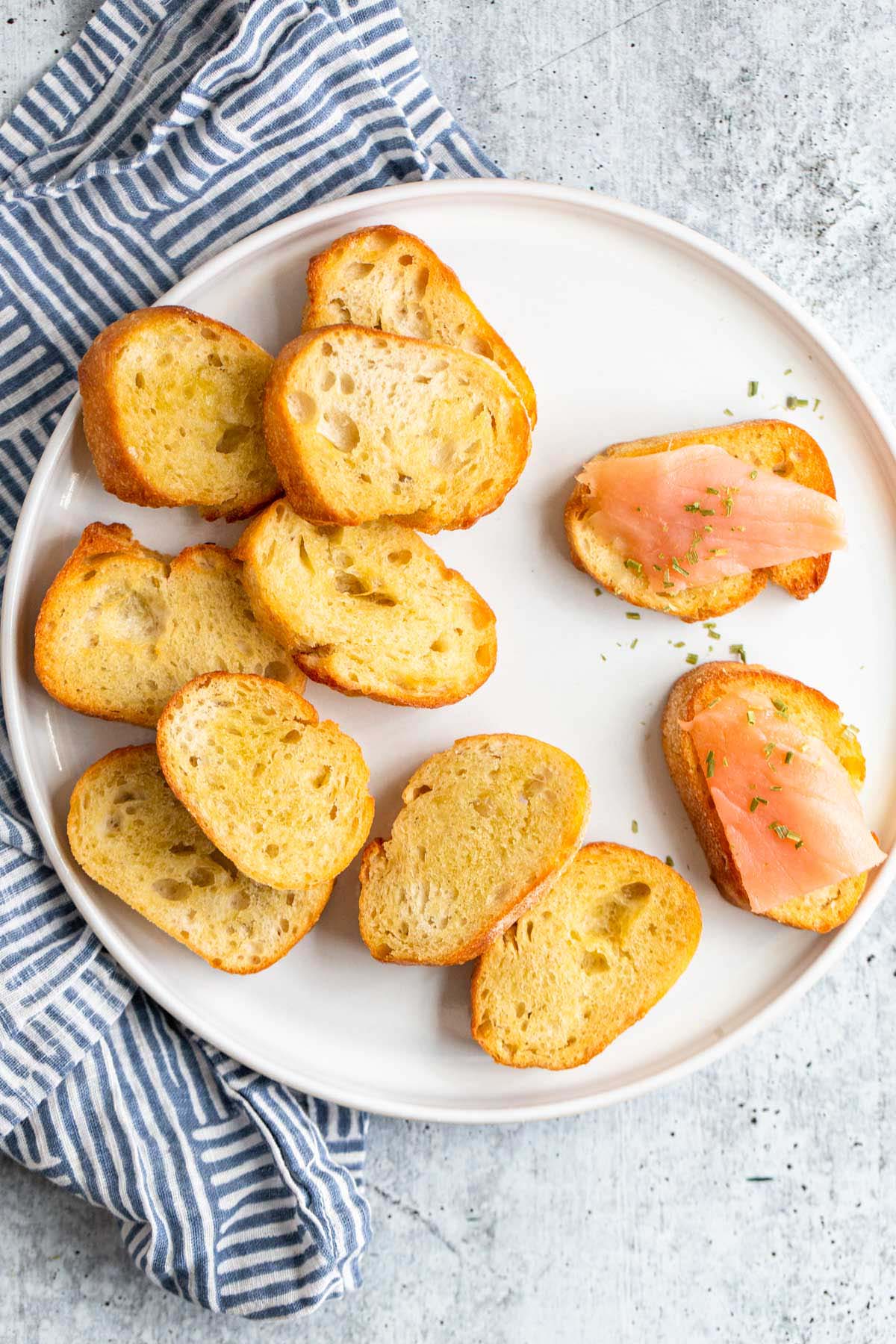 Crostini on a white plate with a white and blue towel.