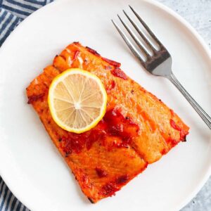 Harissa salmon on a white plate with a slice of lemon.