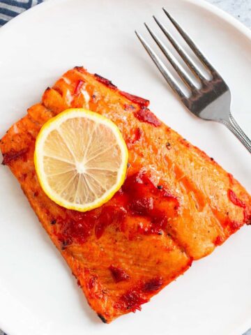 Harissa salmon on a white plate with a slice of lemon.
