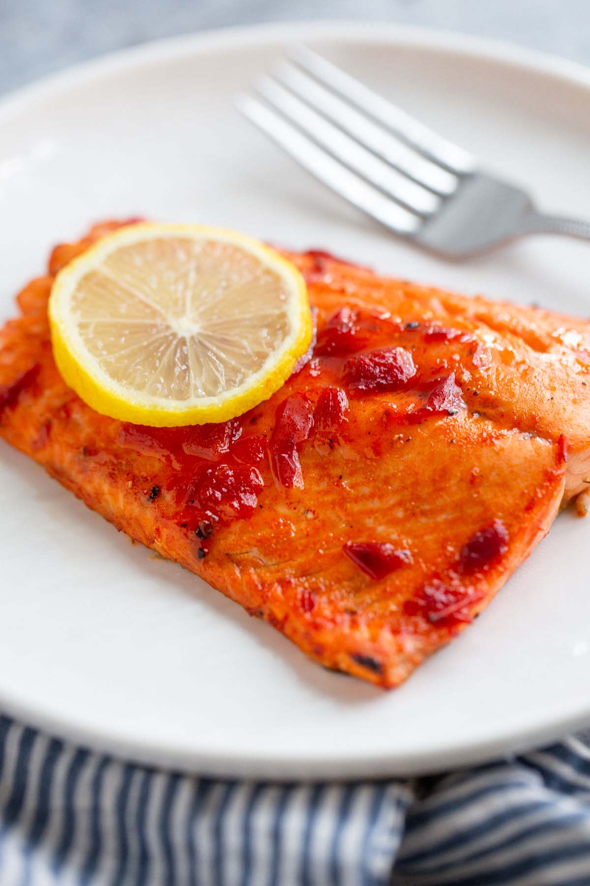 Harissa salmon on a white plate with a lemon slice.