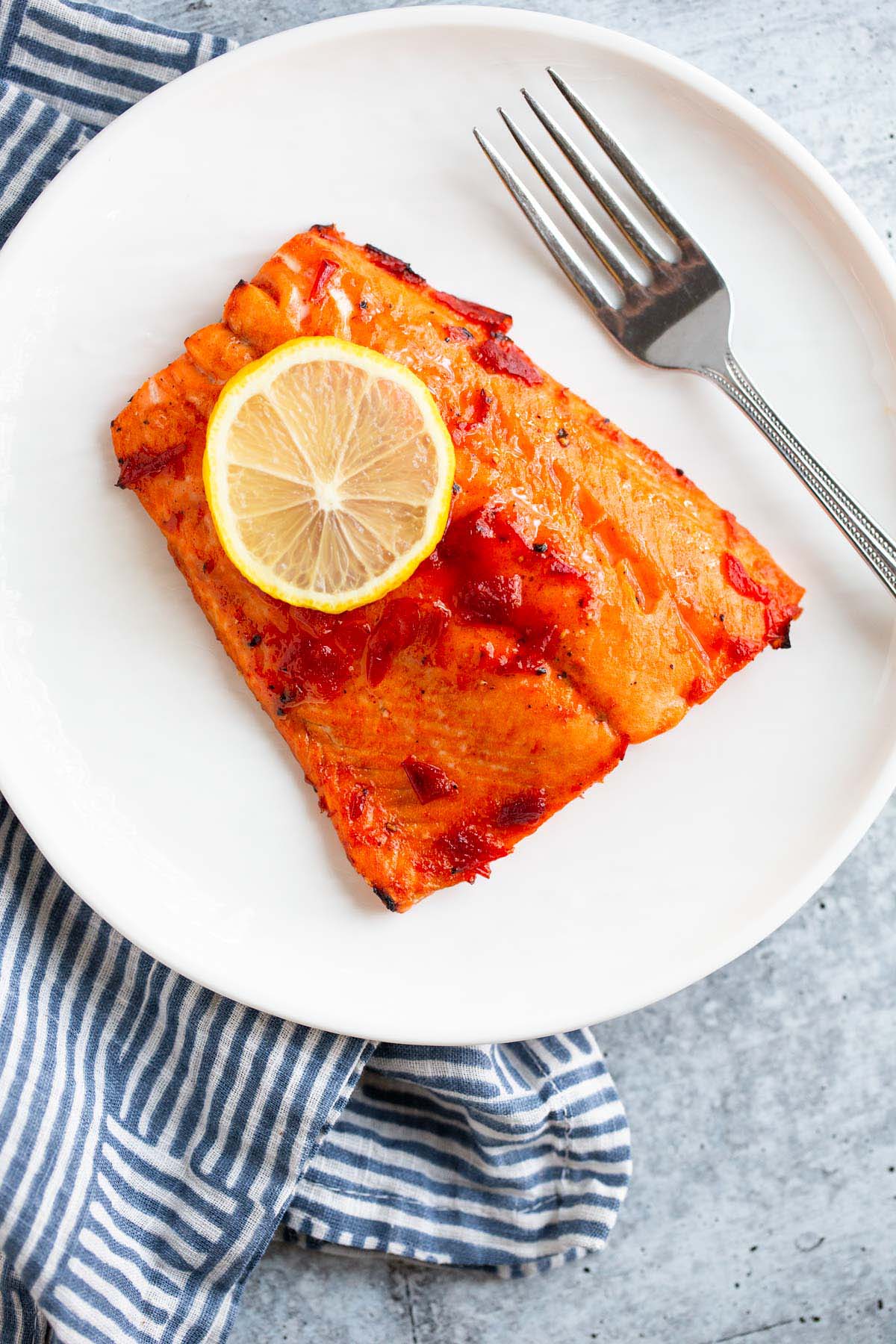 Harissa salmon on a white plate with a lemon slice.