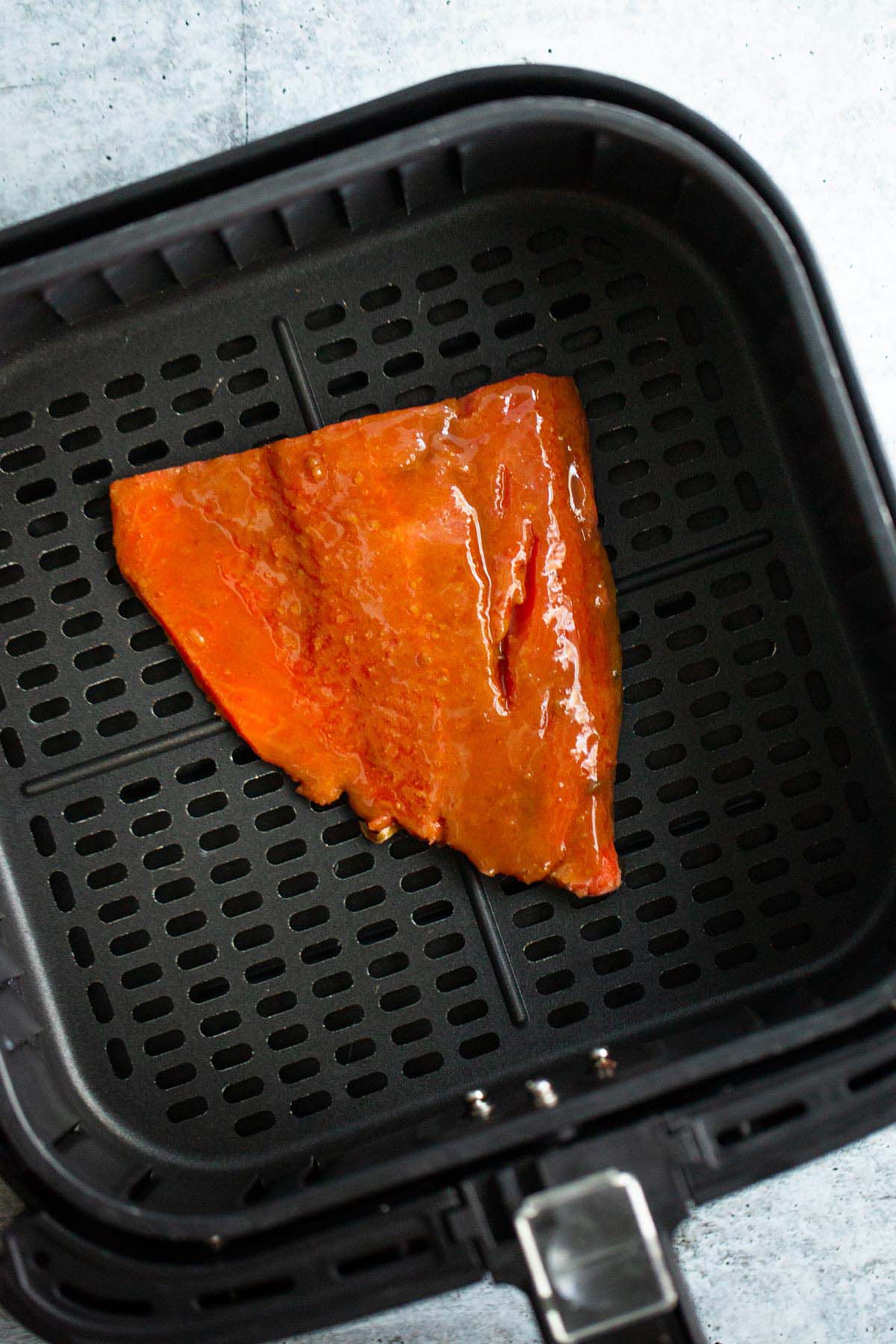 Uncooked miso glazed salmon in air fryer basket.