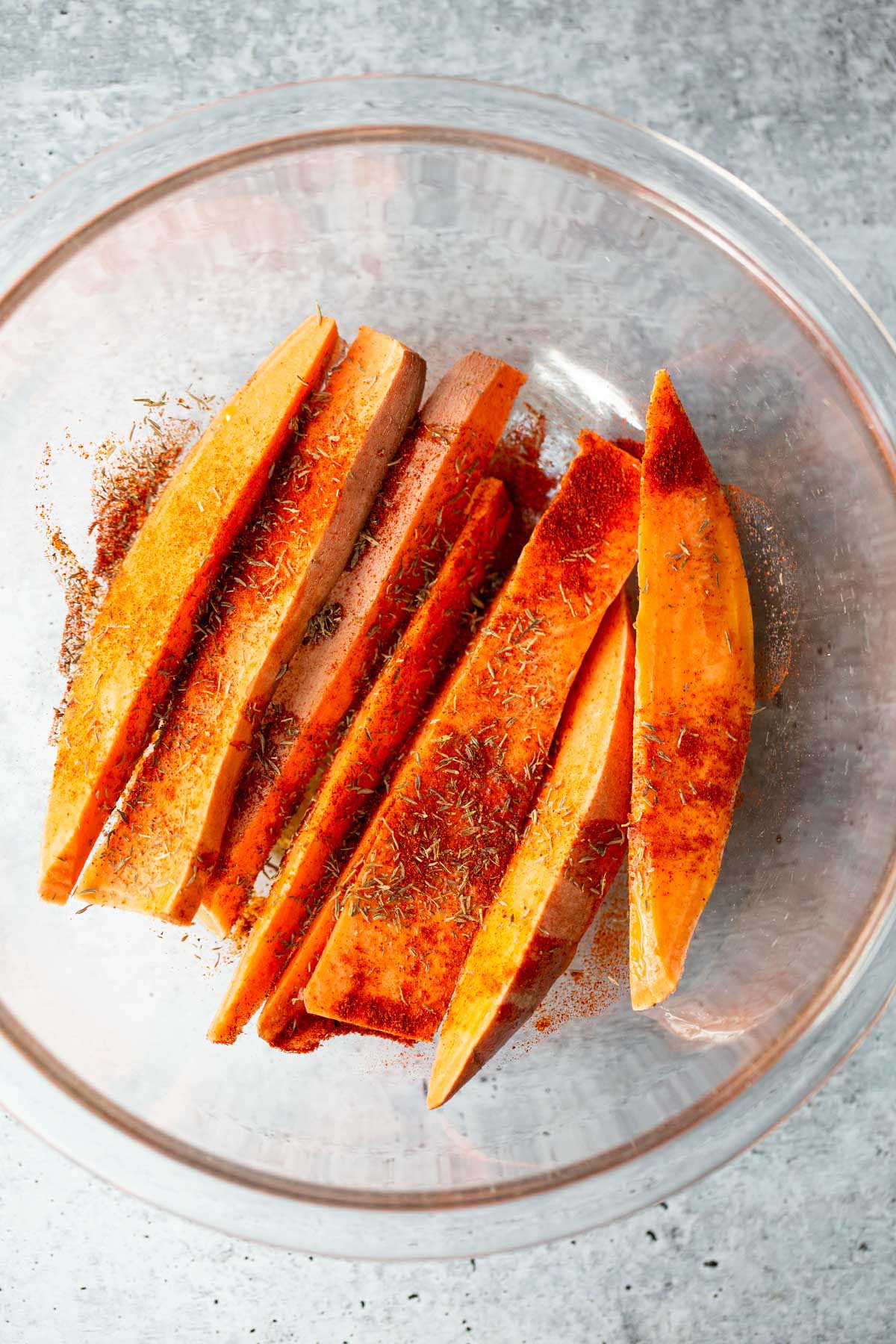 Sweet potato wedges with seasonings in a bowl.
