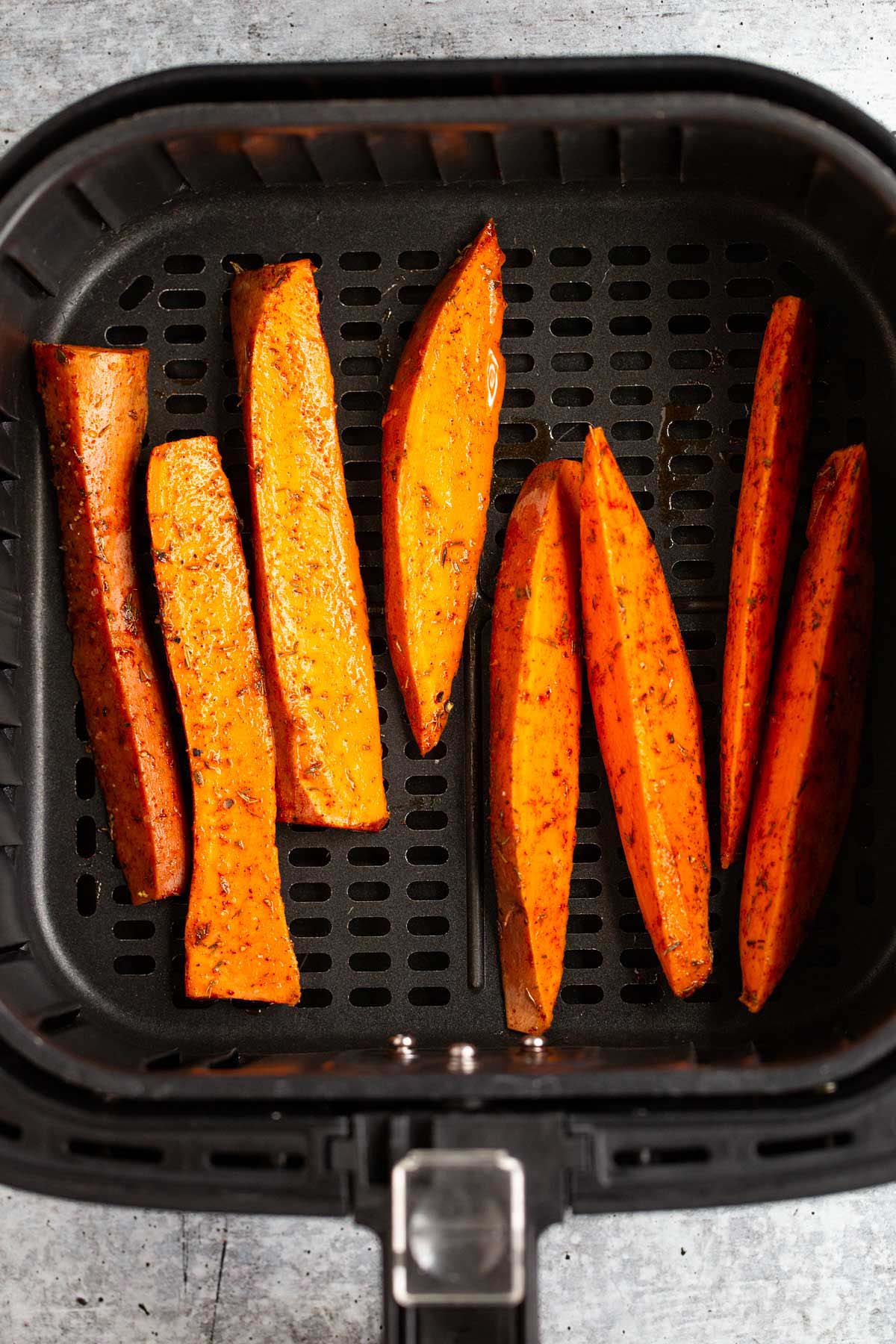 Raw sweet potato wedges in air fryer basket.