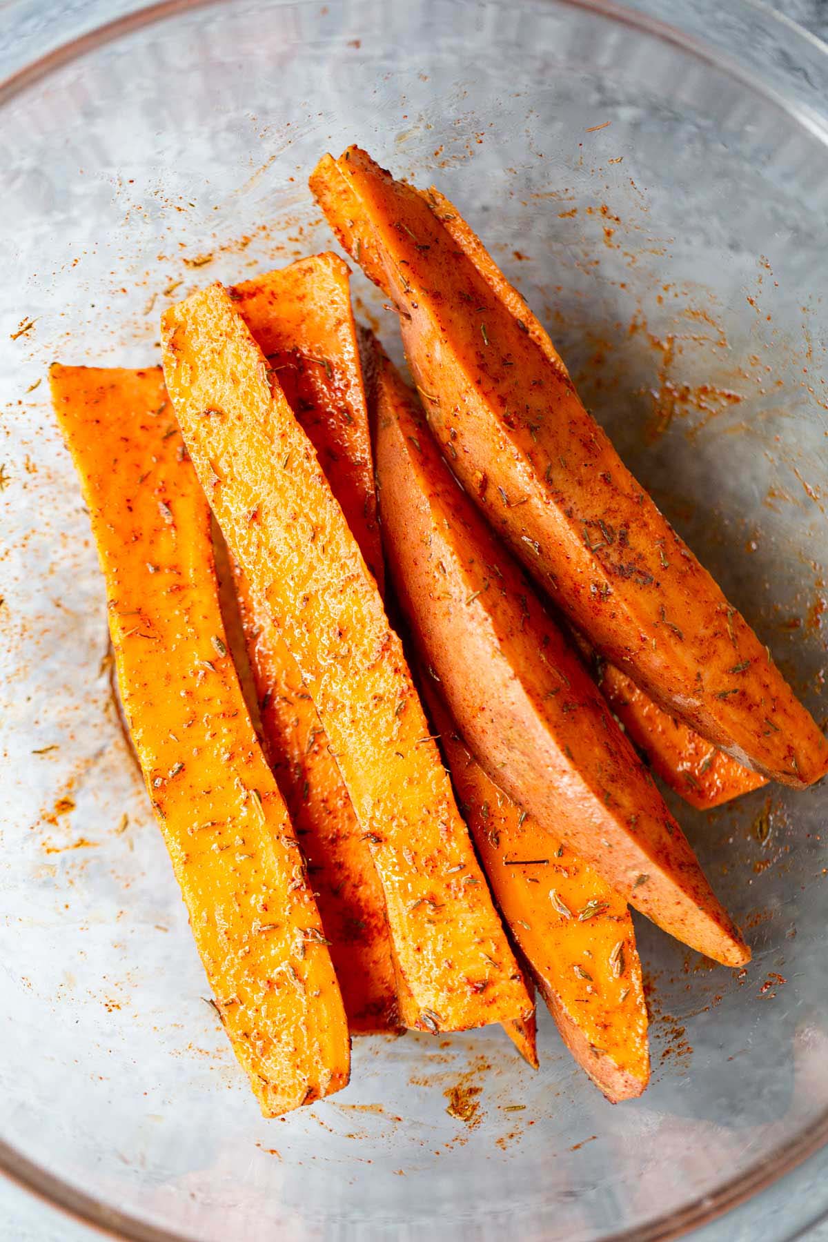 Sweet potato wedges with seasonings in a bowl.