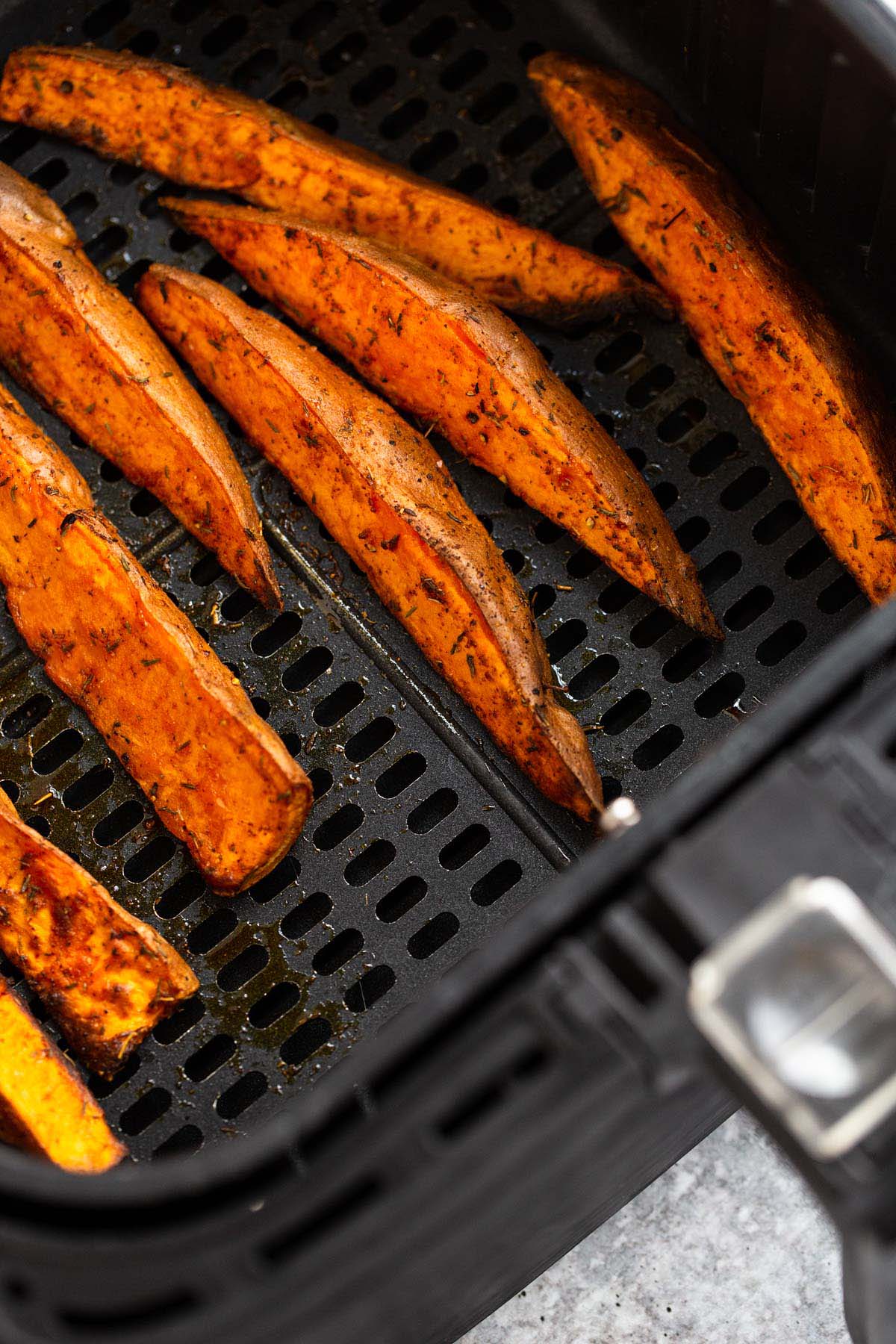 Cooked sweet potato wedges in air fryer basket.