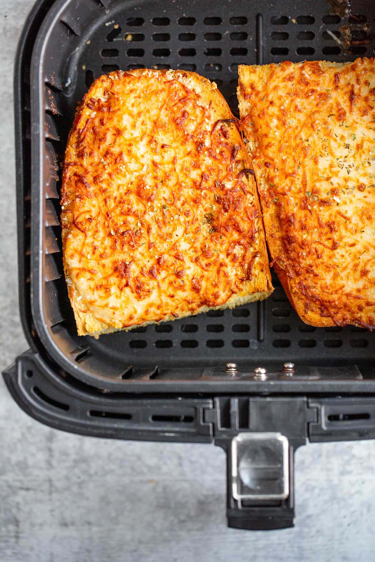 Cooked cheesy garlic bread in air fryer basket.