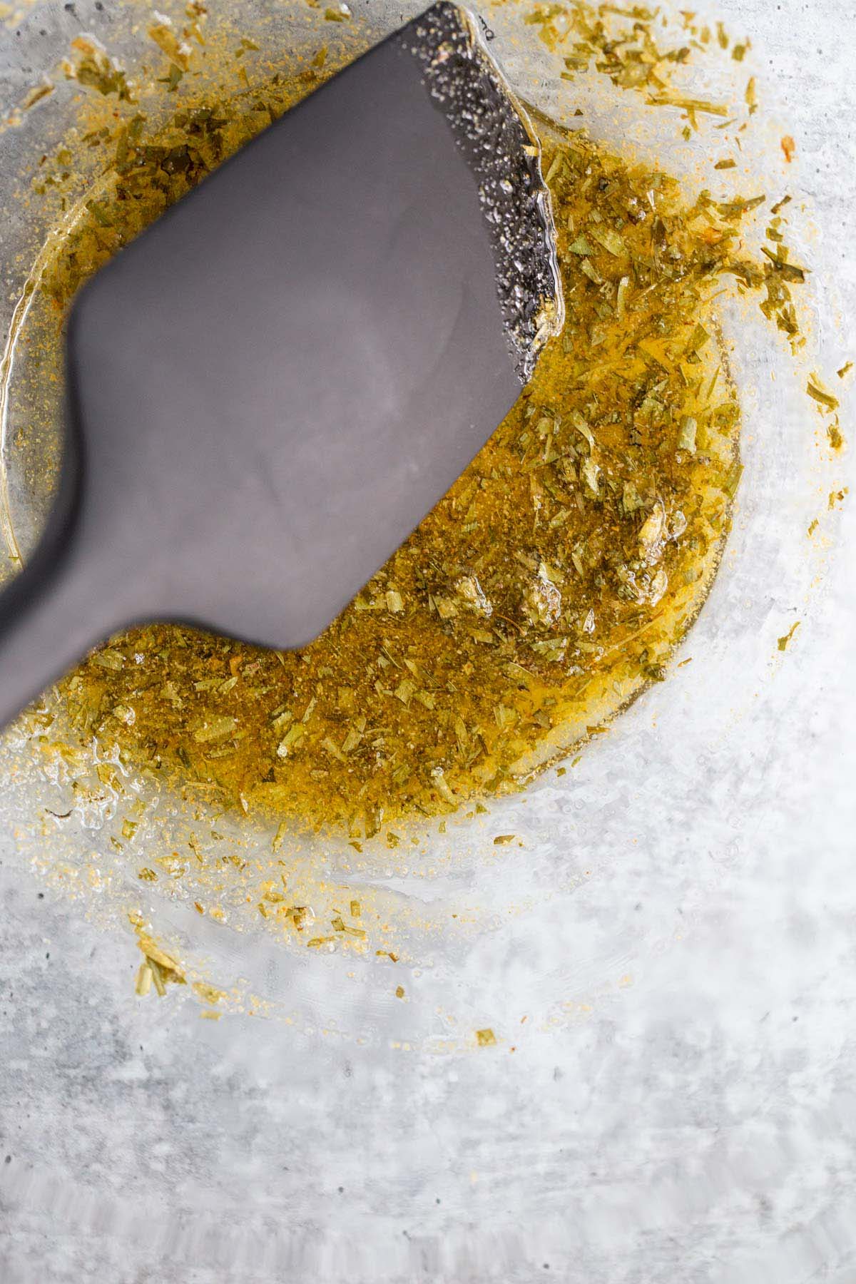 Seasonings, herbs, and oils mixed together in a bowl.