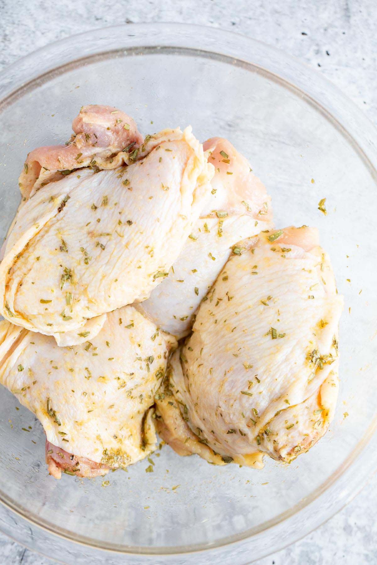 Chicken thighs in a bowl with seasonings.