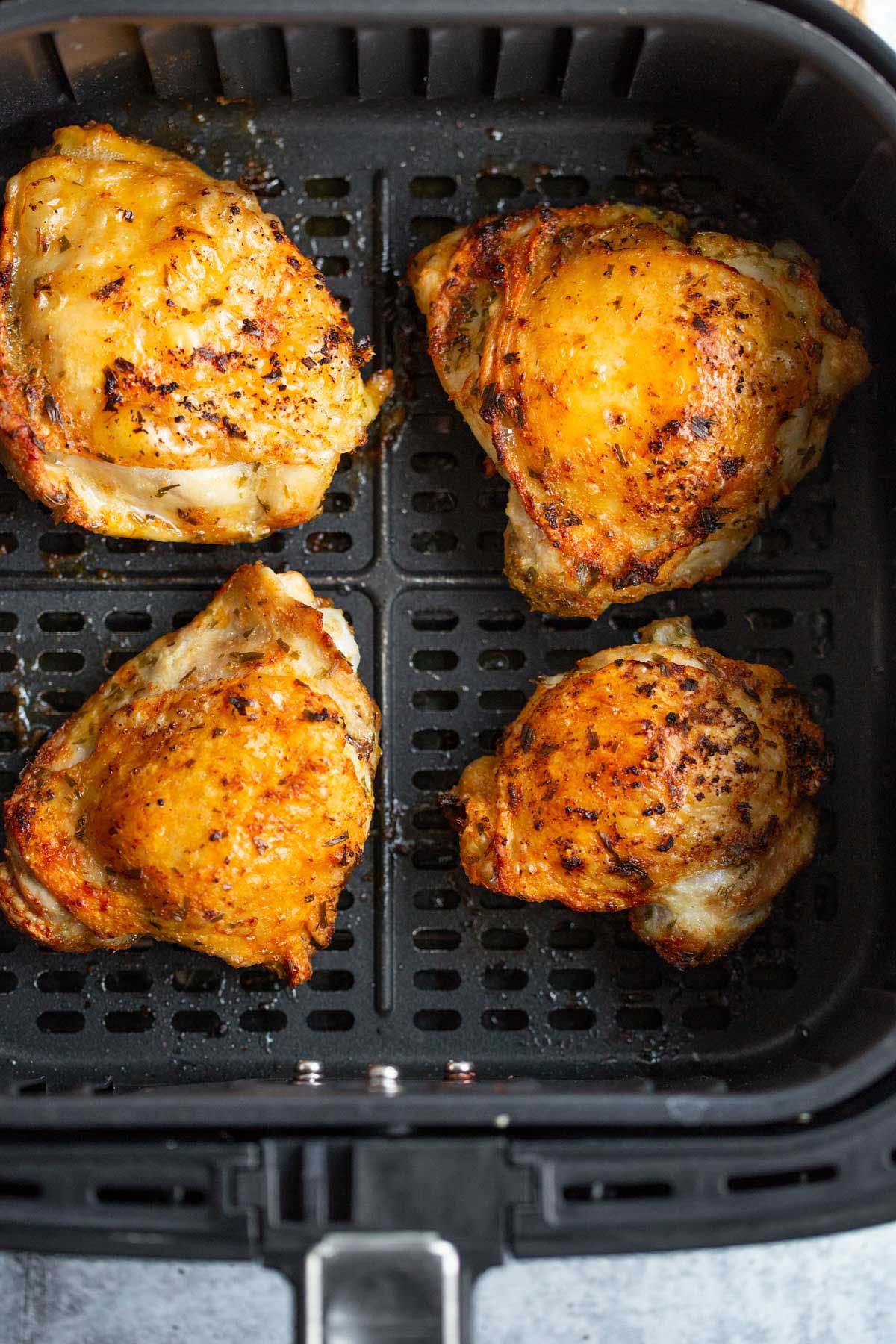 Chicken thighs with crispy skin in air fryer basket.