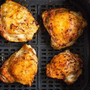 Air fryer crispy chicken thighs in air fryer basket.