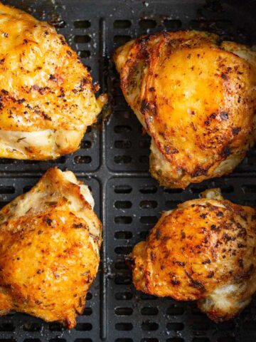 Air fryer crispy chicken thighs in air fryer basket.