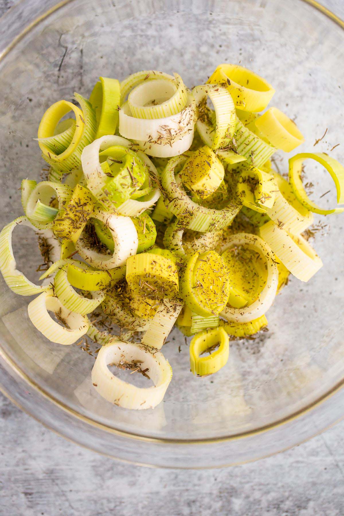 Leeks in a bowl with oil and herbs.