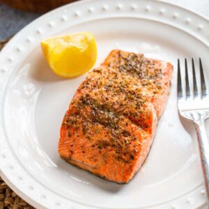 Mediterranean salmon on a plate with a fork and lemon wedge.