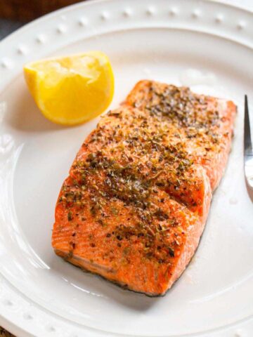 Mediterranean salmon on a plate with a fork and lemon wedge.