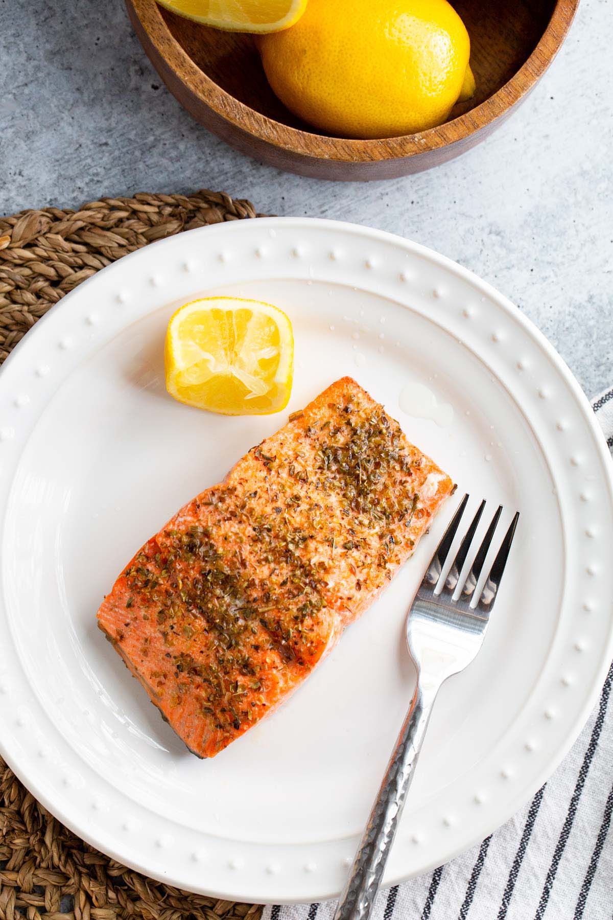 Cooked salmon on a plate with lemon wedge.