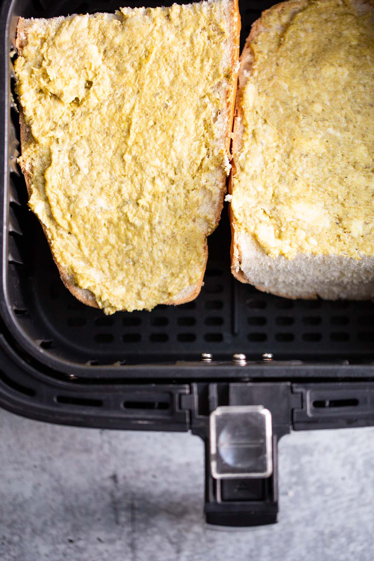 Uncooked pesto garlic bread in air fryer basket.