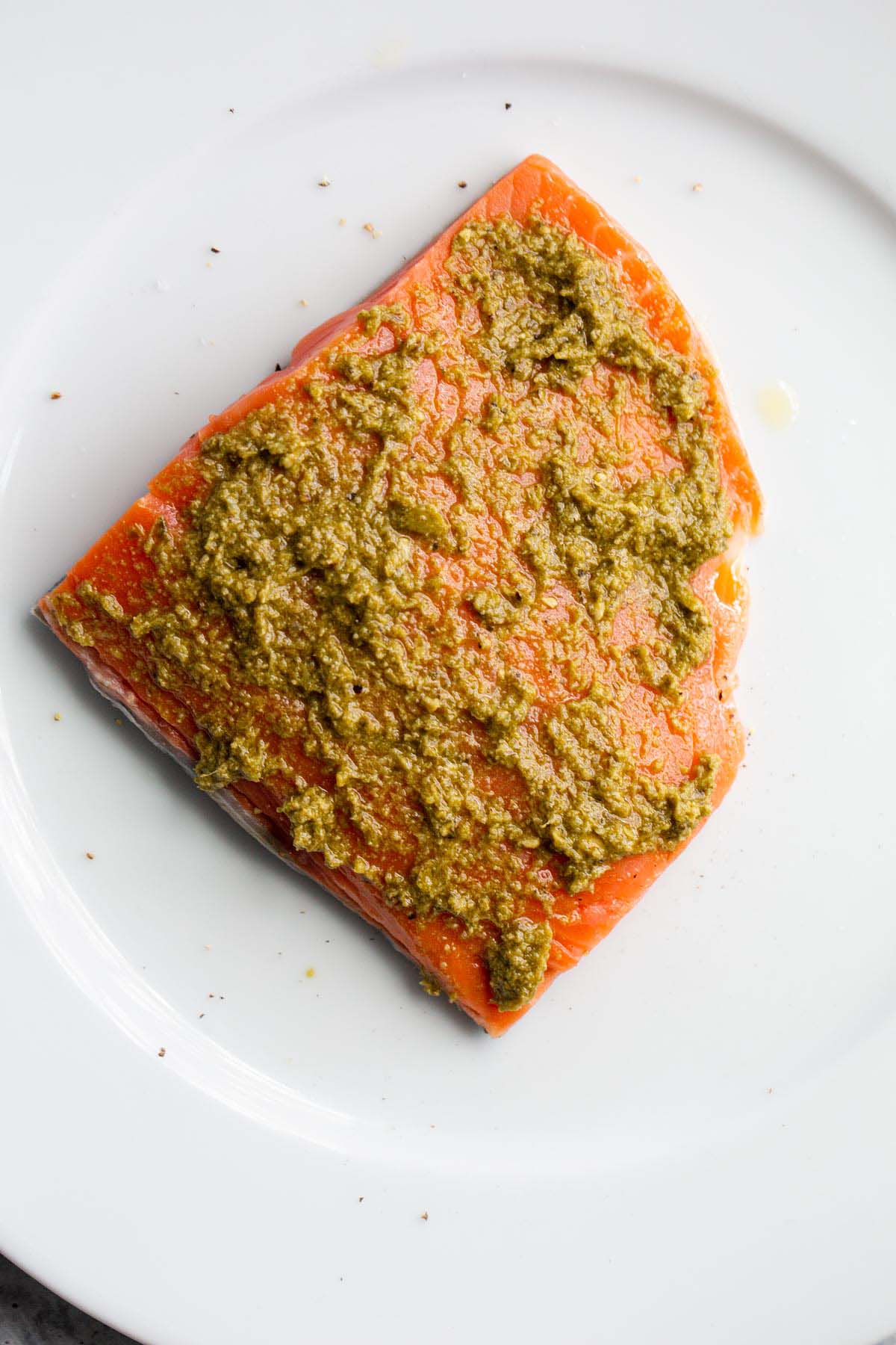Uncooked salmon on white plate with pesto sauce on top.