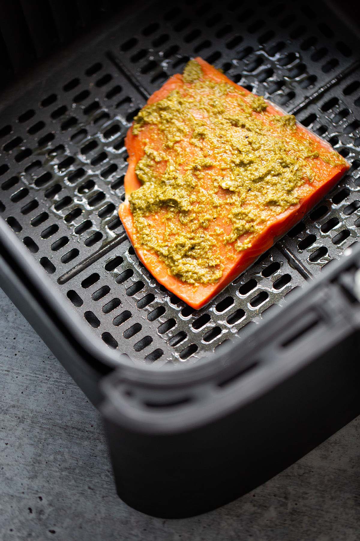 Uncooked salmon in air fryer basket.