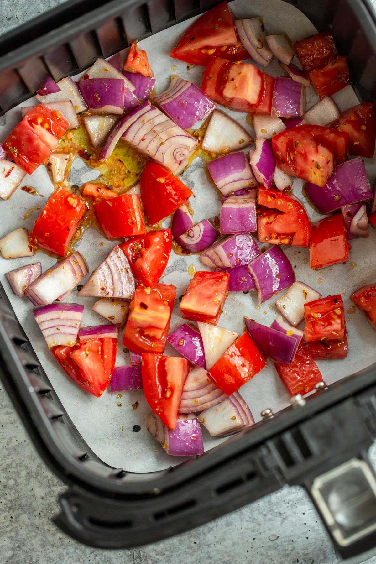 Uncooked tomatoes and onions in air fryer basket.