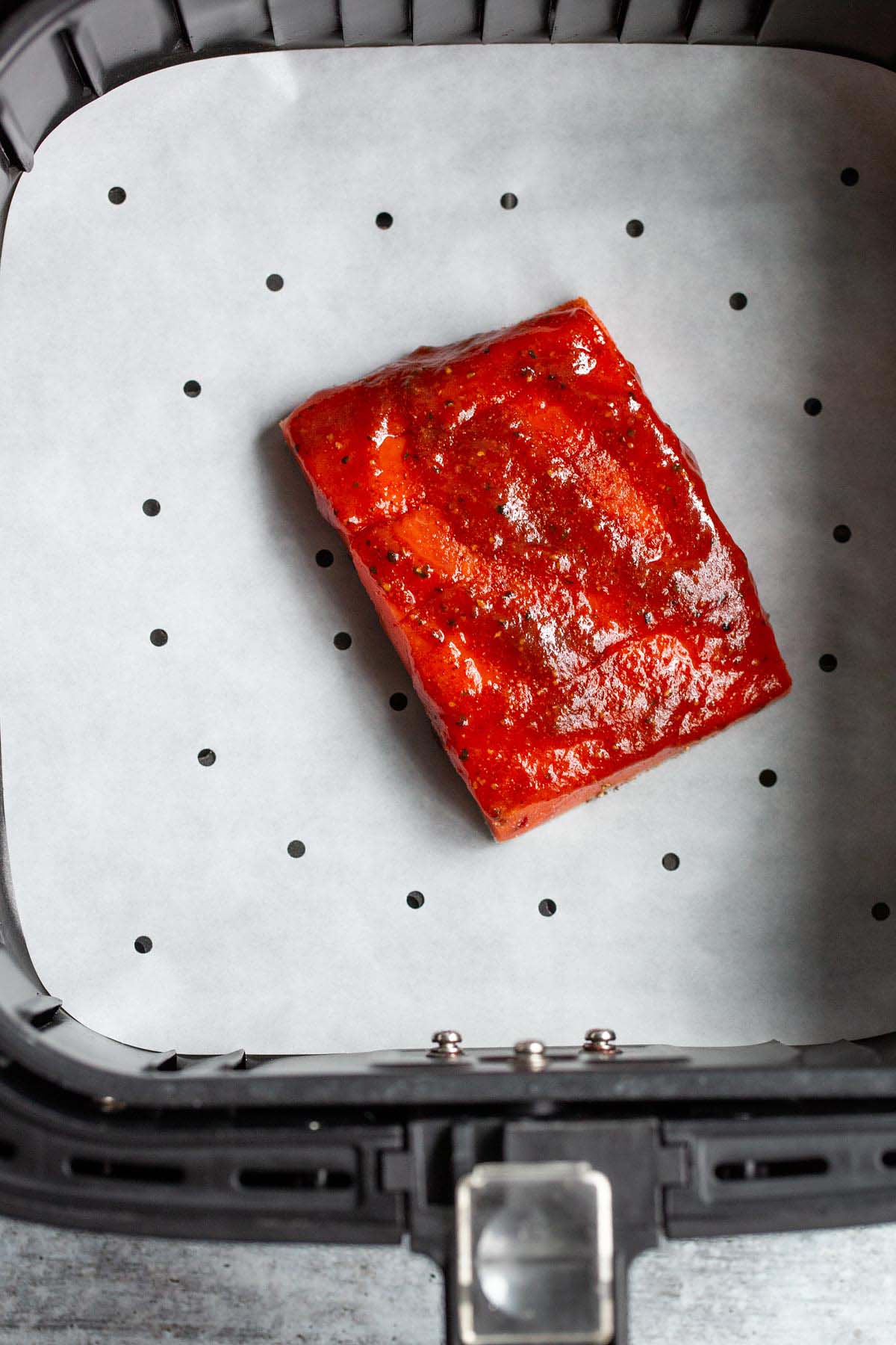 Uncooked bbq salmon in air fryer basket.