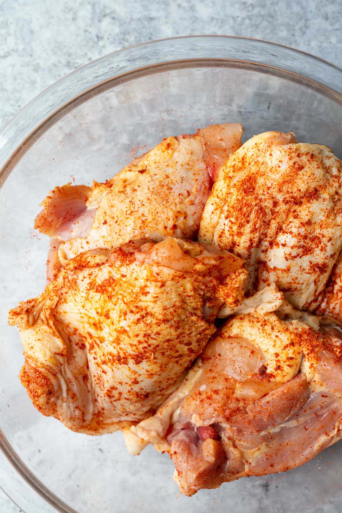 Raw chicken thighs in a bowl with seasonings.