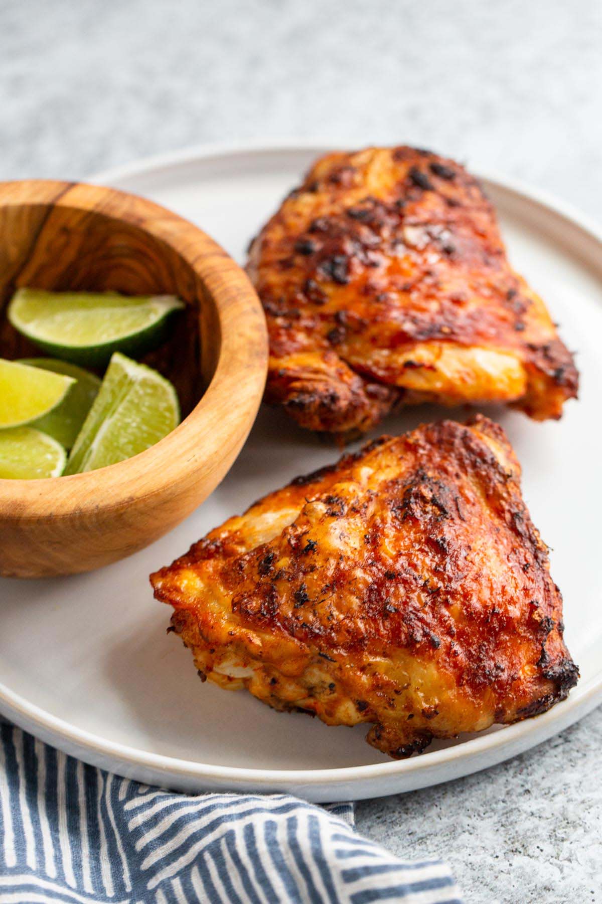 Peri peri chicken thighs on a white plate with limes on the side.