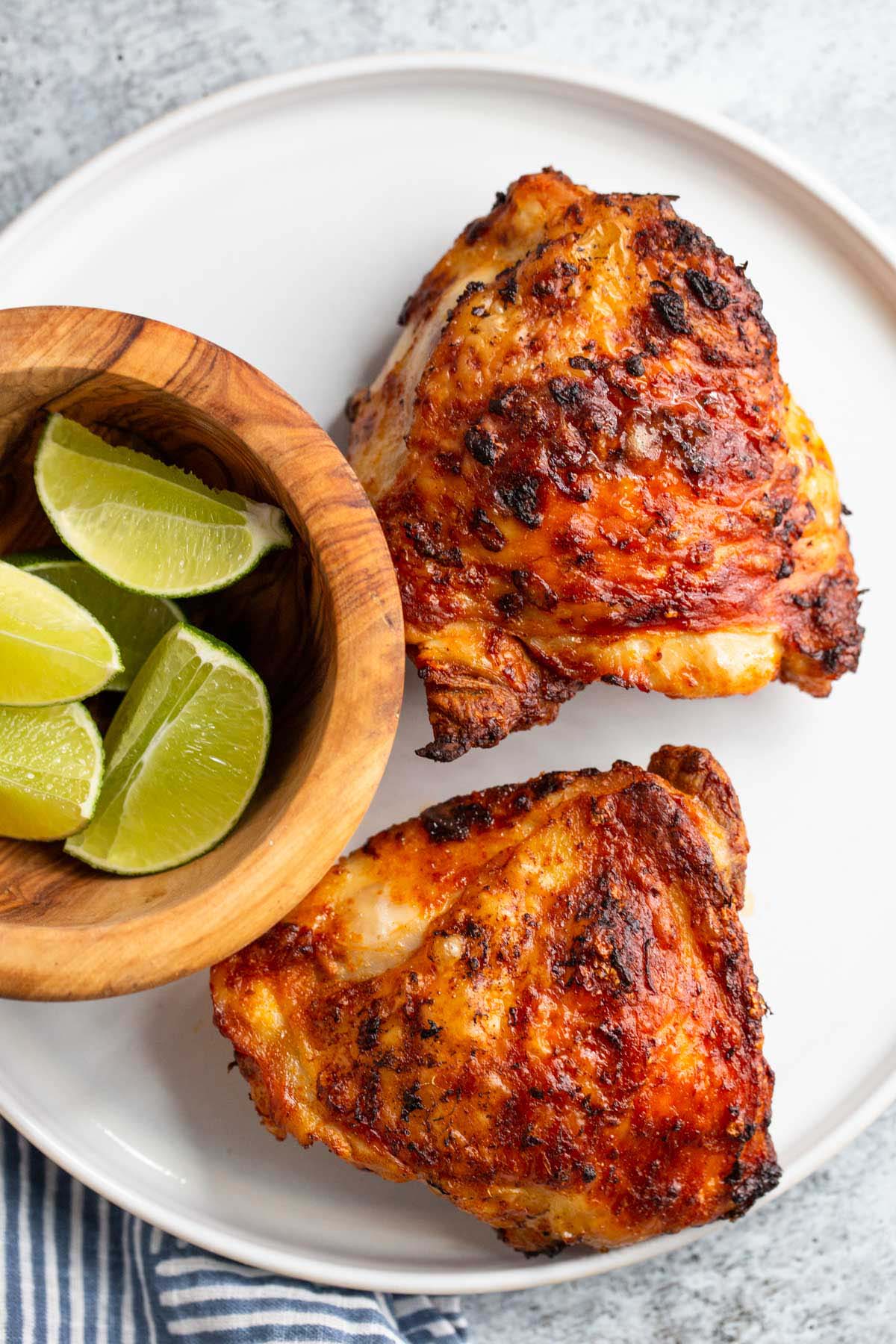 Peri peri chicken thighs on a white plate with limes on the side.