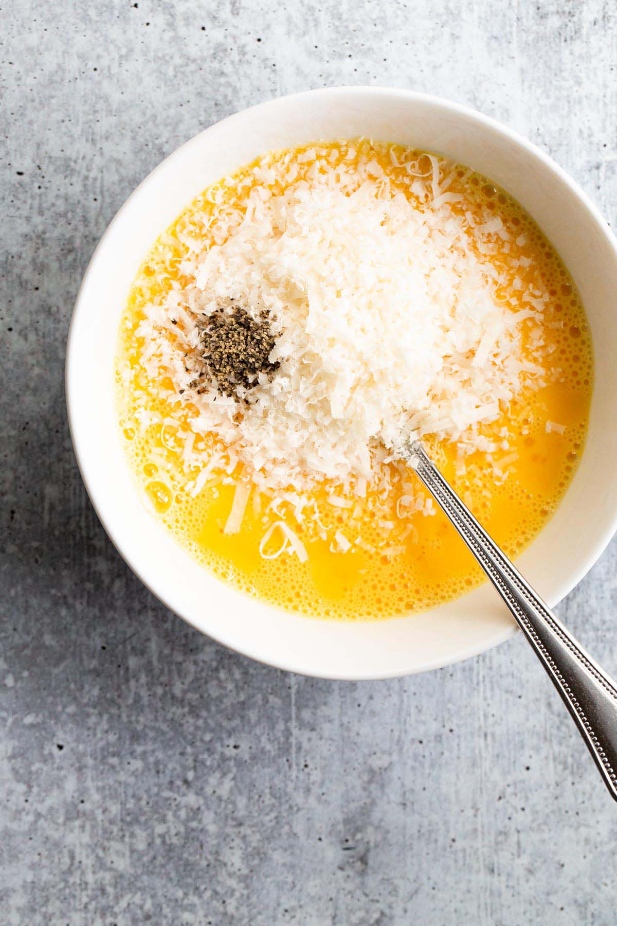 Scrambled eggs in a bowl with parm and black pepper.