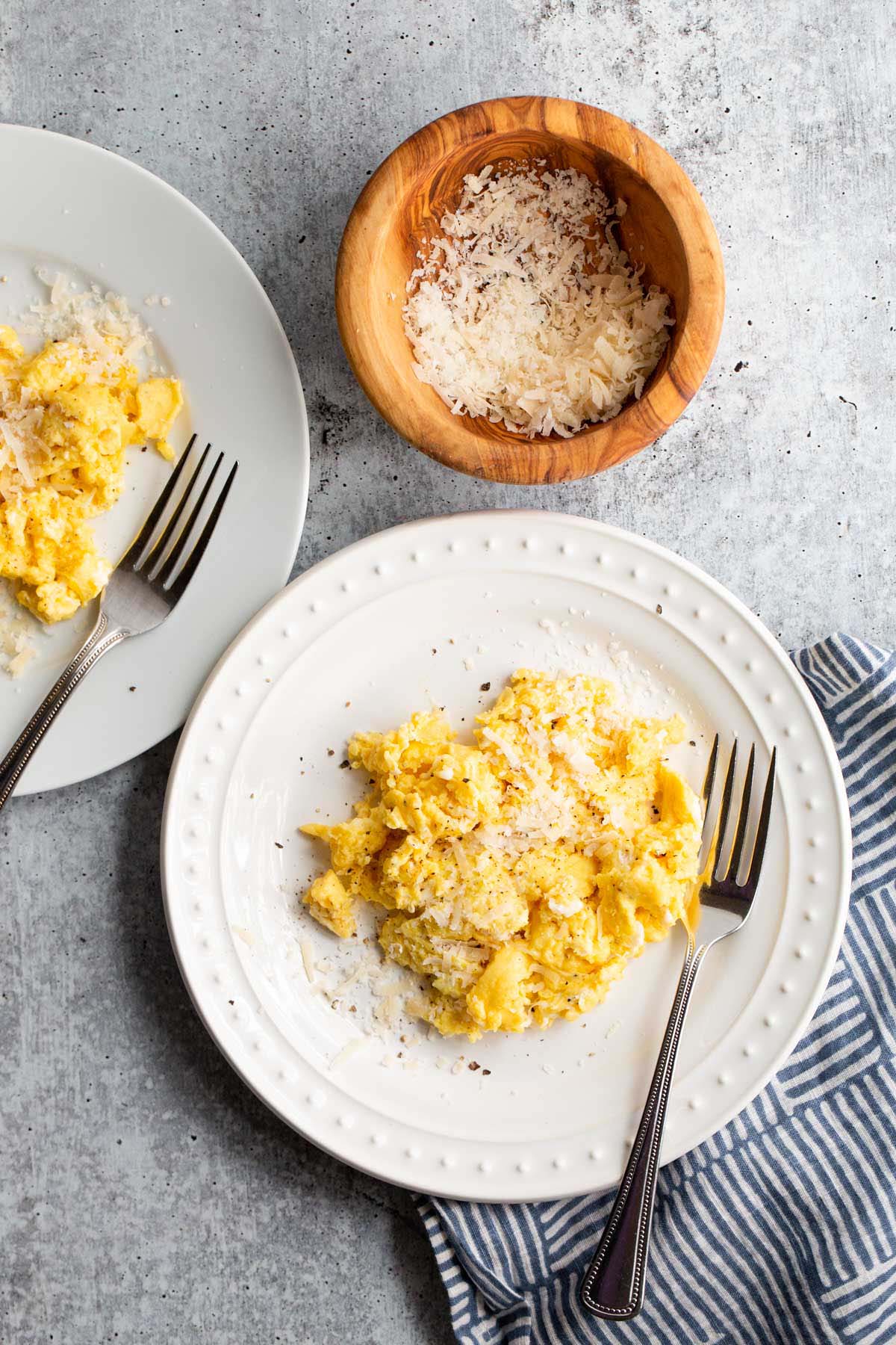 Two plates of cacio e pepe eggs with a bowl of parmesan cheese.