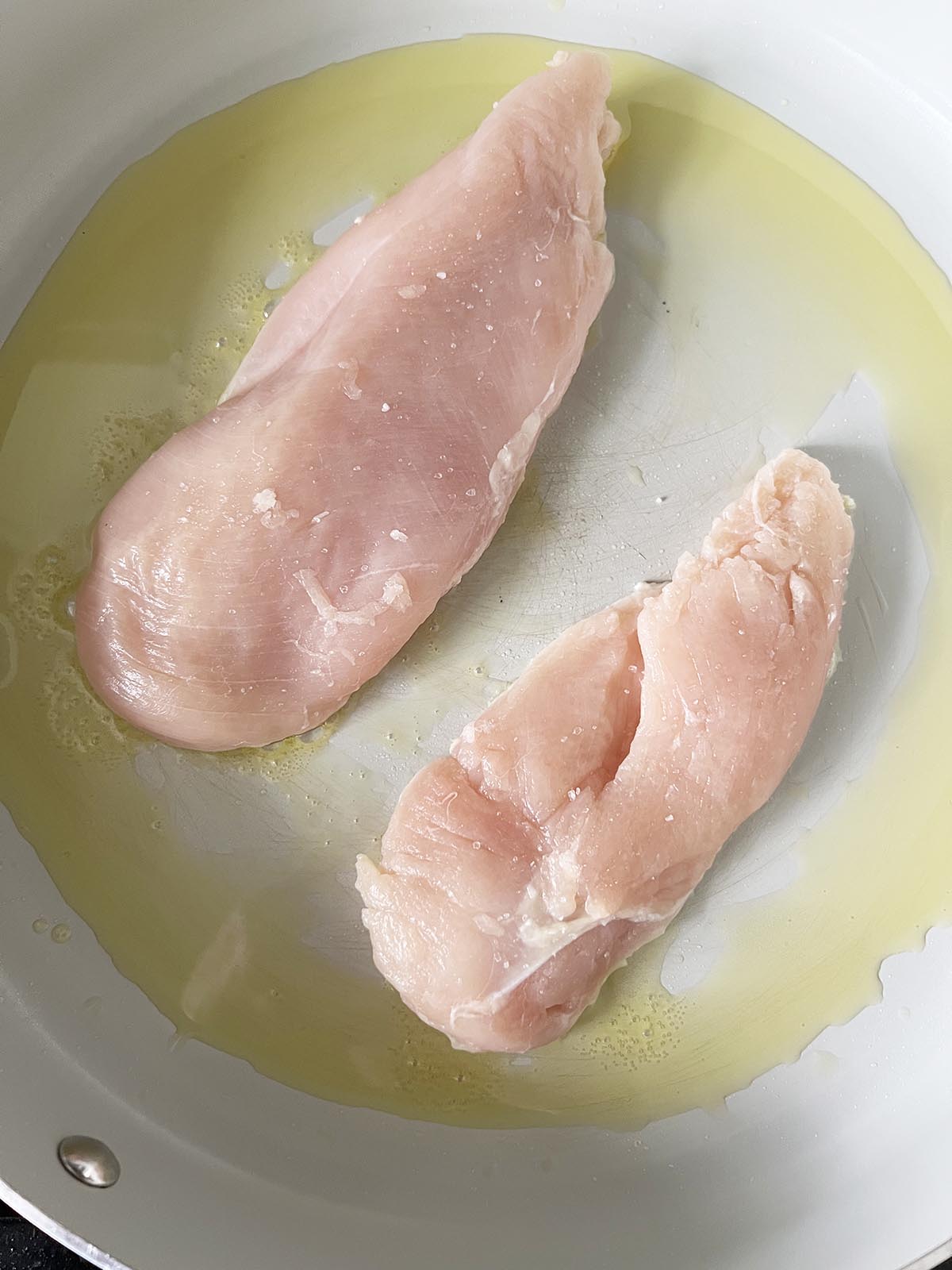 Chicken breast cooking in a skillet.