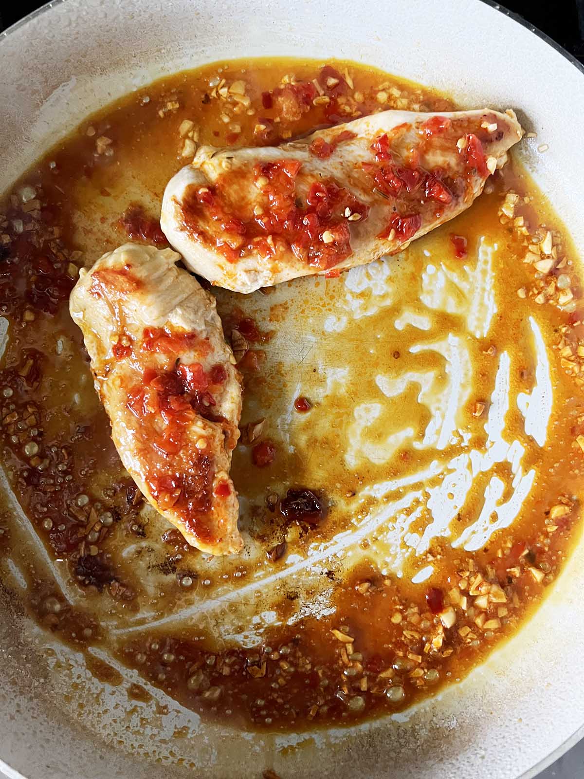 Chicken cooking in a skillet with calabrian sauce.