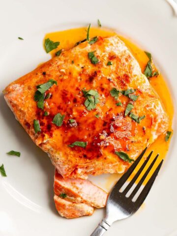 Peri Peri Salmon on a white plate with parsley on top.