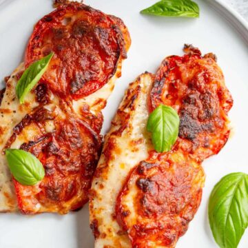 Air fried caprese chicken on a white plate topped with basil leaves.