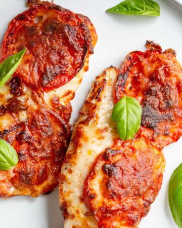 Air fried caprese chicken on a white plate topped with basil leaves.