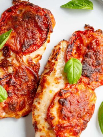 Air fried caprese chicken on a white plate topped with basil leaves.