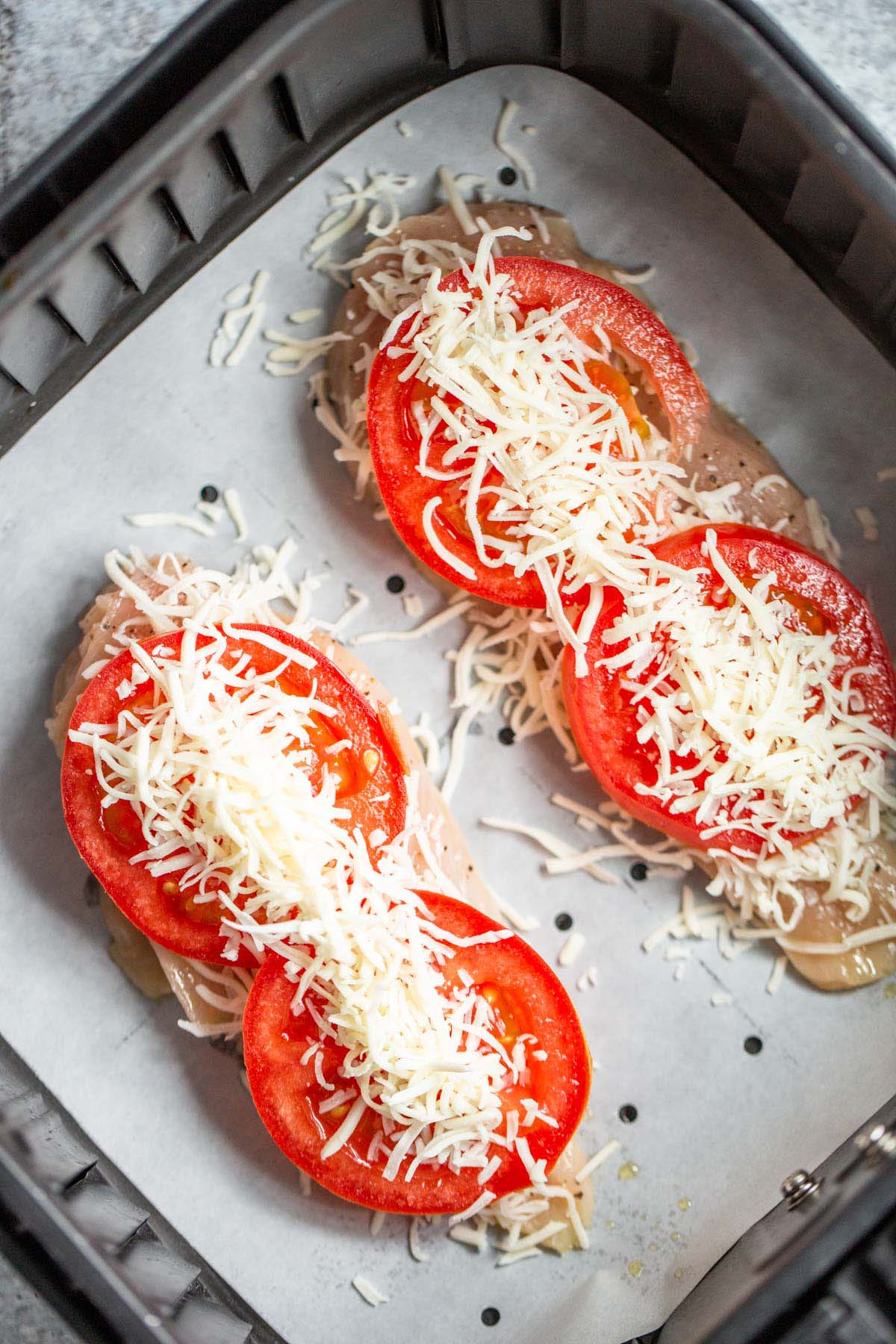 Topping chicken and tomatoes with cheese before cooking.