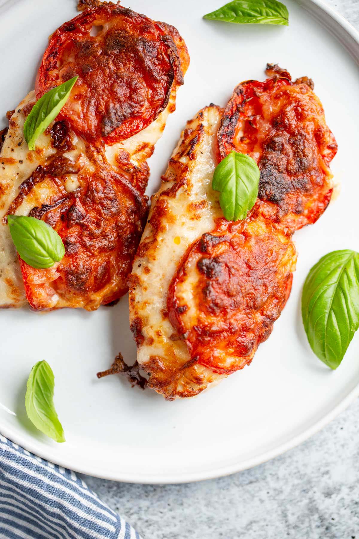 Air fryer caprese chicken on a plate with basil leaves.