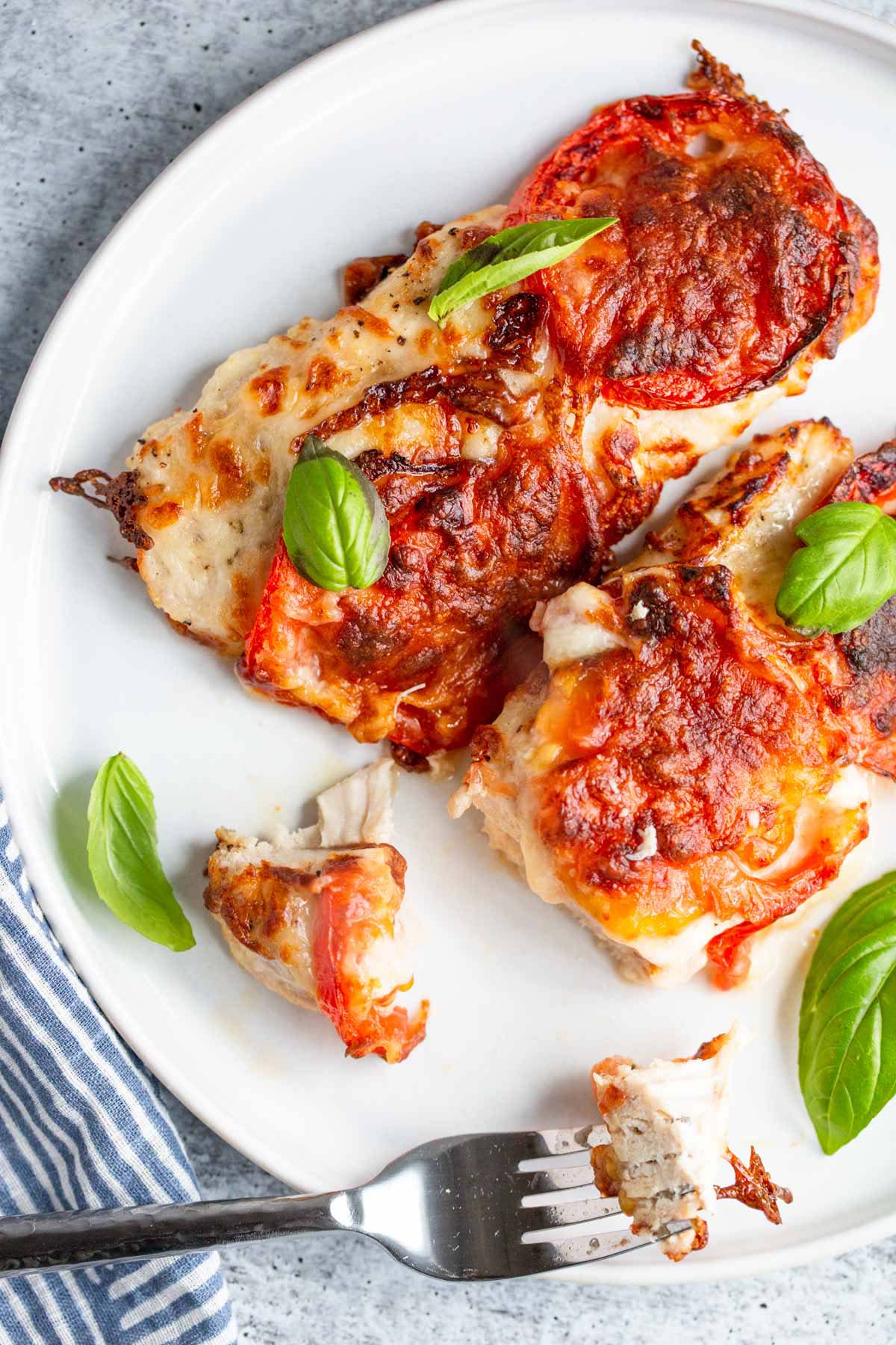 Air fryer caprese chicken on a plate with basil leaves.