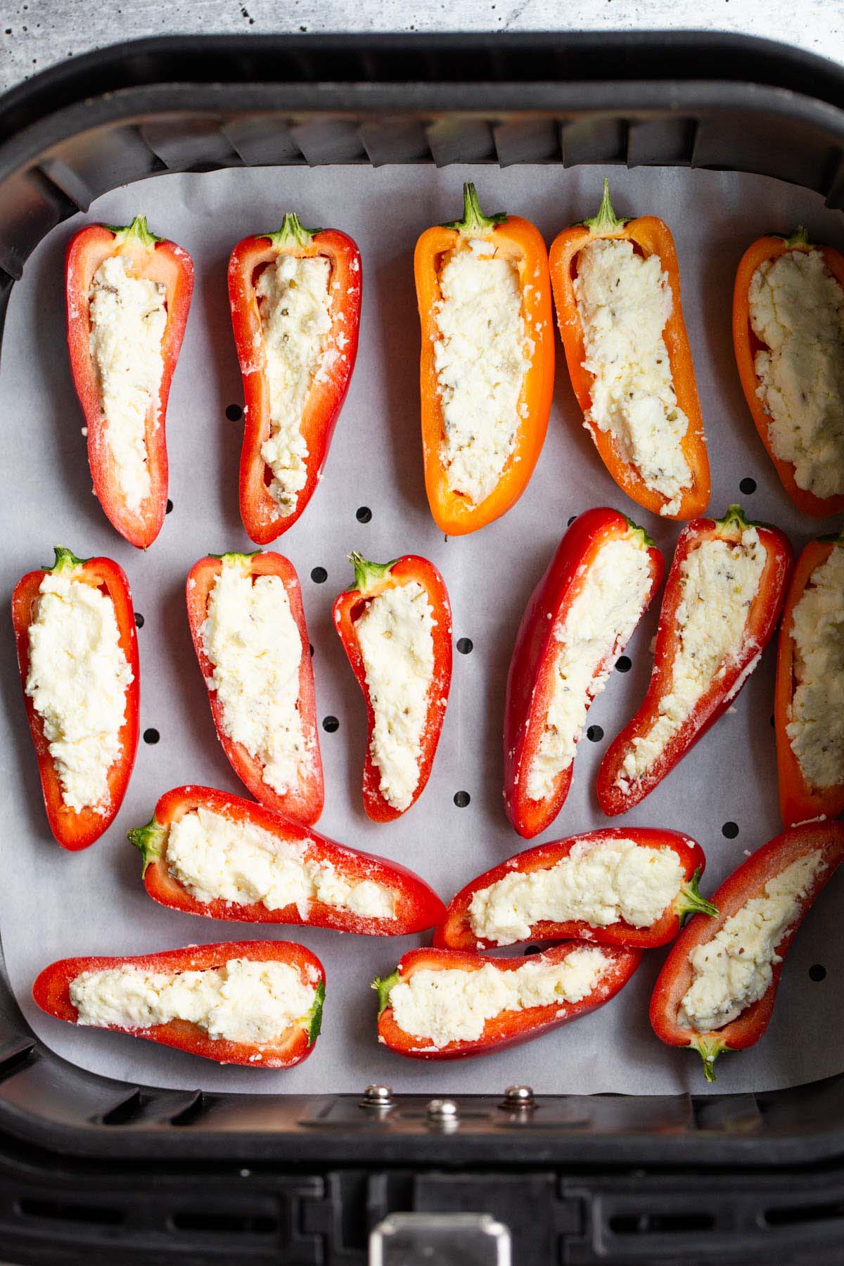 Uncooked feta stuffed mini peppers in air fryer basket.