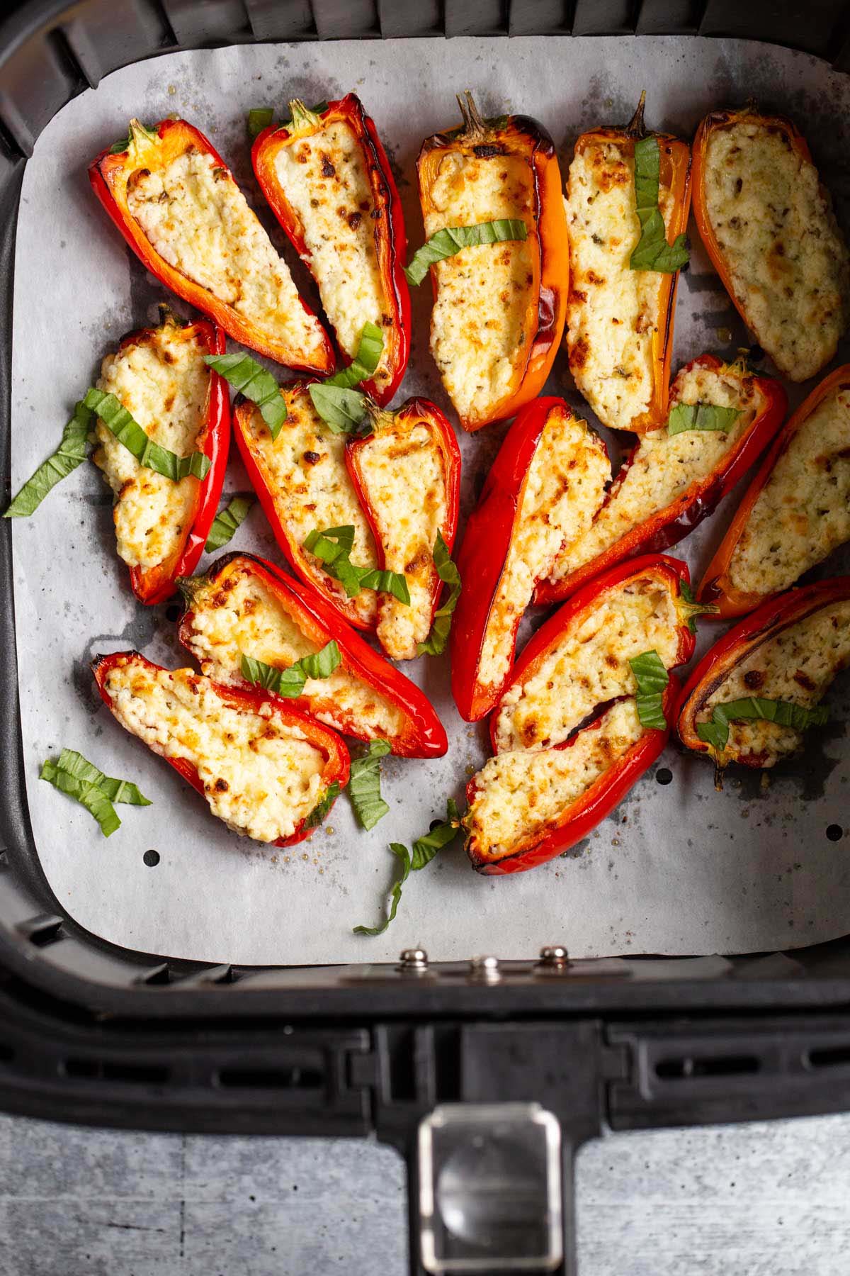 Feta stuffed mini peppers topped with basil in air fryer basket.