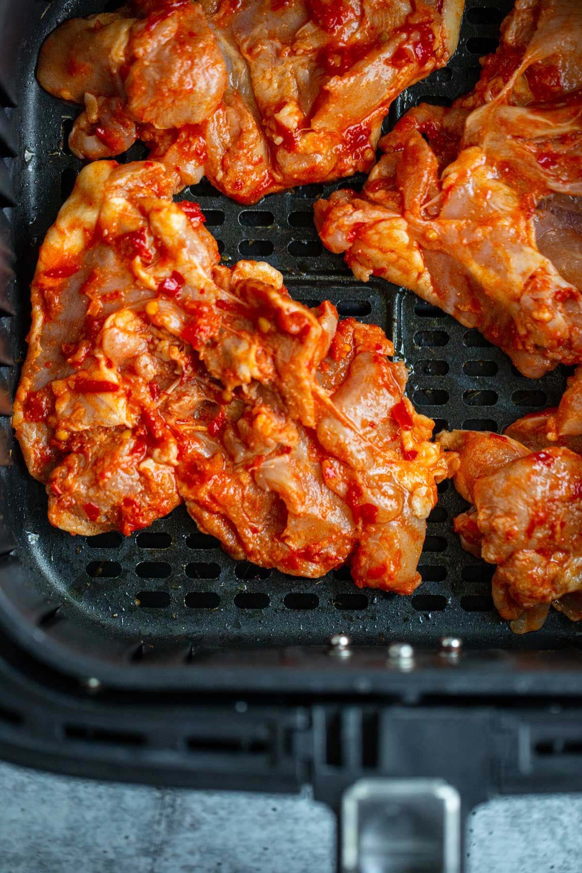 Uncooked chicken in air fryer basket.