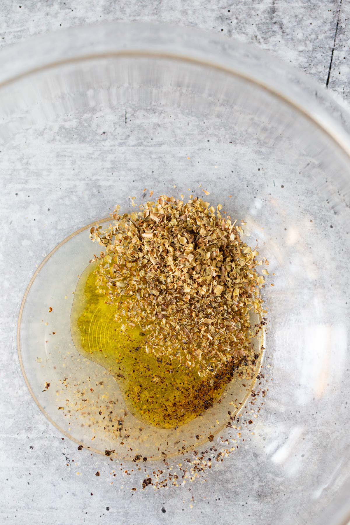 Olive oil, lemon juice, and herbs in a glass bowl.