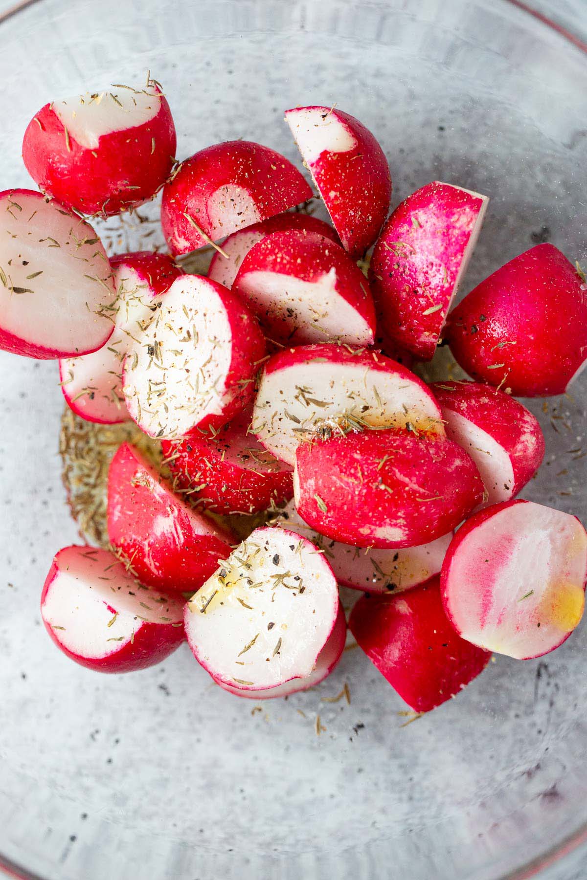 Radishes in a bowl with oil and herbs.